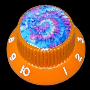 May include: A round orange control knob with a ribbed side and a flat top featuring a blue, purple, and pink tie-dye pattern. The base of the knob displays white printed numbers ranging from one to ten in a circular arrangement around the edge.