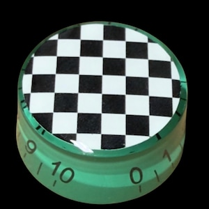 May include: A translucent green circular control knob featuring a black and white checkered pattern on its top surface. The side of the knob displays black numerical markings ranging from zero to ten, indicating a graduated scale for adjustment.