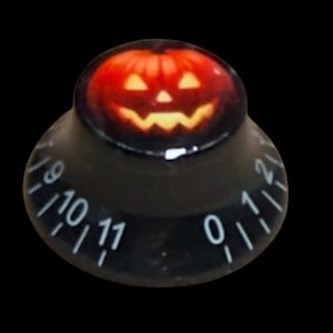 Puede incluir: Un mando de control cónico negro con un gráfico impreso de una calabaza de Halloween naranja brillante en la parte superior. El lateral del mando muestra marcas numéricas blancas del cero al once, dispuestas en un patrón circular en la base.