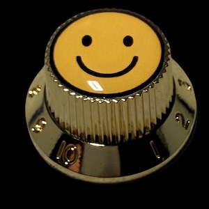 May include: A gold-colored control knob with a yellow smiley face in the center. The knob has a ridged edge and numbers 1 through 10 around the perimeter. The background is black.