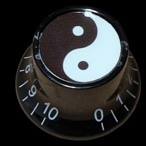 May include: A black cylindrical control knob featuring a white and black yin-yang symbol on the top surface. The side of the knob is marked with white numerical indicators ranging from zero to ten, arranged in a circular pattern around the base.