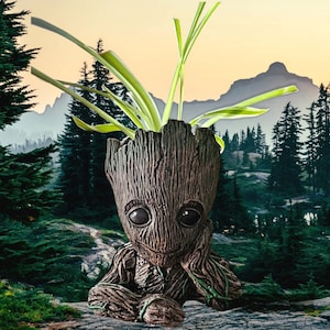 Pode incluir: Um vaso de cerâmica marrom e cinza em forma de personagem de um filme de ficção científica popular. O vaso tem uma cabeça grande com um sorriso largo e olhos grandes. O vaso está cheio de uma planta verde com folhas longas e finas.