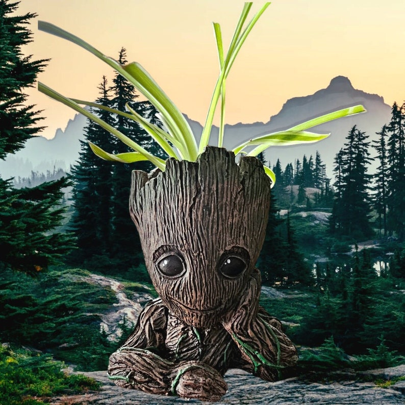May include: A brown and grey ceramic planter shaped like a character from a popular science fiction film. The planter has a large head with a wide smile and large eyes. The planter is filled with a green plant with long, thin leaves.