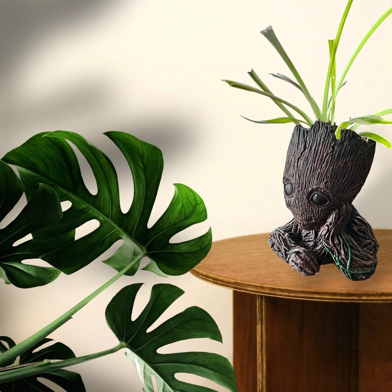 May include: A brown and green ceramic planter shaped like a character from a popular science fiction film. The planter is sitting on a wooden table with a green leafy plant growing out of the top.
