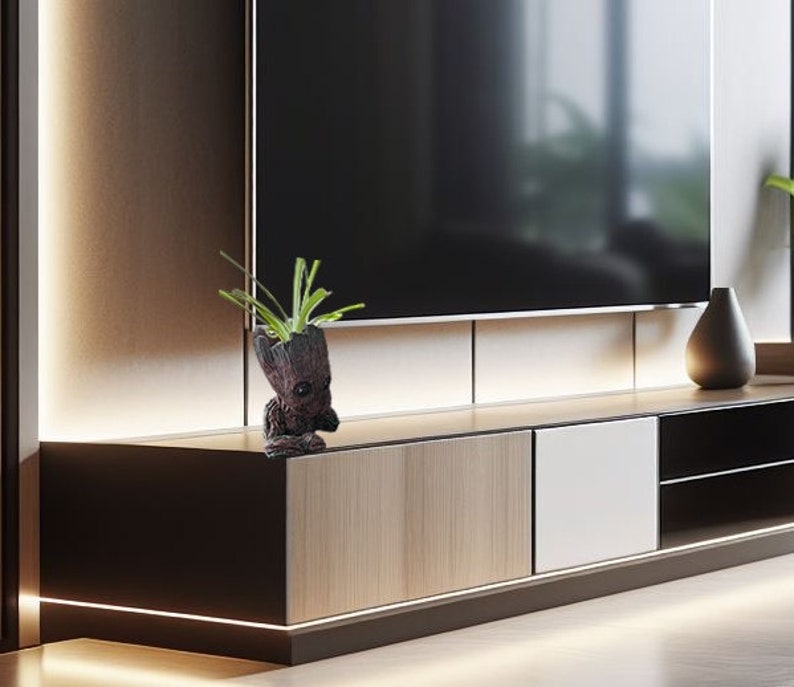 May include: A small, brown, potted plant with green leaves sits on a wooden shelf. The plant is shaped like a character from a popular film. The shelf is part of a modern entertainment unit with a flat screen TV mounted above it.