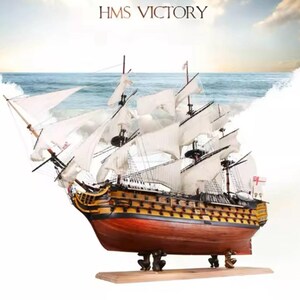 May include: A detailed model of the HMS Victory, a historic British warship. The model is made of wood and features white sails, a brown hull, and a wooden base. The ship's name, "HMS Victory", is printed on the base.