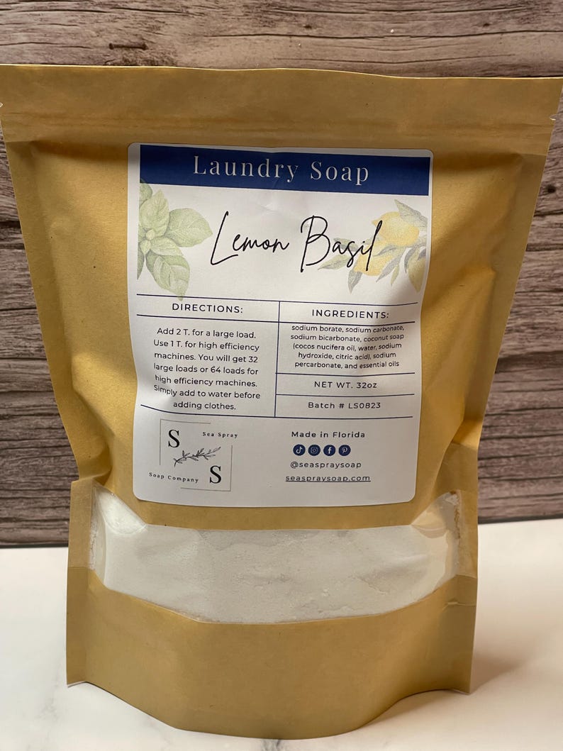 Op de afbeelding: Een bruine papieren zak met Lemon Basil wasmiddel. Het etiket bevat de tekst "Laundry Soap" en "Lemon Basil". De ingredi&euml;nten en instructies staan vermeld. Het nettogewicht is 907g. De merknaam is Sea Spray Soap Company.