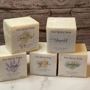 May include: Five square bars of Sea Spray Soap, each wrapped in white paper. The labels feature botanical illustrations and the scents: Lemon Basil, Unscented, Lavender, Fresh Citrus, and Lemongrass. Each bar is XXL and weighs 13.6 oz.