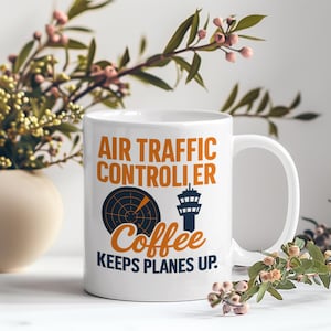 May include: White ceramic mug with the text "AIR TRAFFIC CONTROLLER Coffee KEEPS PLANES UP." The mug features a radar graphic and a control tower illustration in navy blue and orange. A perfect gift for air traffic controllers.