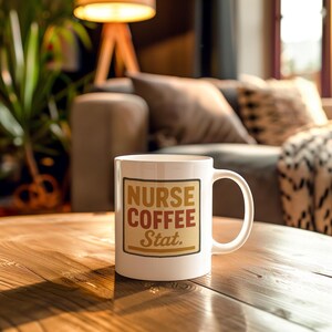 May include: White ceramic mug featuring the text "NURSE COFFEE Stat." in a rectangular design. The text is in brown and red shades. The mug is placed on a wooden table.