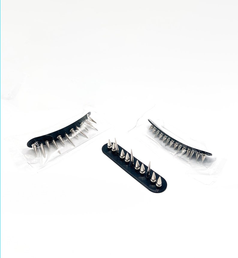 May include: Three black hair accessories with silver-colored spikes. Two are curved, and one is straight. The accessories are packaged in clear plastic on a white background. The spikes are evenly spaced.