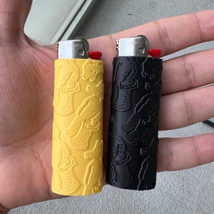 Puede incluir: Dos encendedores con un diseño texturizado. Un encendedor es amarillo con un diseño negro y el otro es negro con un diseño blanco.