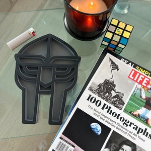 May include: A black ashtray shaped like a Wu-Tang Clan logo. The ashtray is made of a hard, durable material and has a smooth, glossy finish.