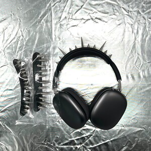 May include: Black over-ear headphones with silver spikes on the headband. A matching black hair comb with silver spikes is also visible. The items are displayed on a crinkled silver surface.