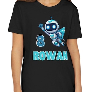 May include: Black t-shirt featuring a cartoon robot with blue and white accents, a blue cape, and the number 8. The name "ROWAN" is printed in blue below the number.