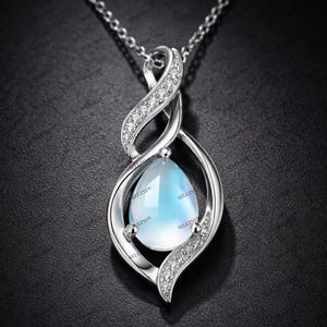 May include: A silver pendant necklace featuring a pear-shaped, light blue gemstone. The pendant is encased in a swirling, openwork design, accented with small, clear crystals. The necklace chain is delicate and silver.