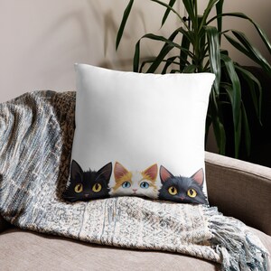 May include: A white throw pillow with three cartoon cats peeking out from behind it. The cats are black, white, and orange.