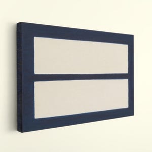 May include: Abstract wall art featuring a navy blue border with two off-white rectangular shapes. The artwork is mounted on a canvas and leans slightly against a white wall, showcasing a modern minimalist design.
