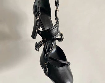 May include: Black leather heeled shoes with multiple straps and buckles. The straps are adorned with silver studs.
