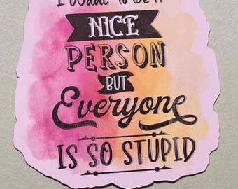 May include: A die-cut sticker with a watercolor background in shades of pink and orange. The black text reads: I Want To Be A NICE PERSON BUT Everyone IS SO STUPID. The design features decorative banners and lines surrounding the lettering.