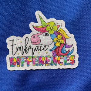 May include: A white sticker with a rainbow unicorn and the text "Embrace Differences". The unicorn has a rainbow mane and tail, and is wearing a flower crown.