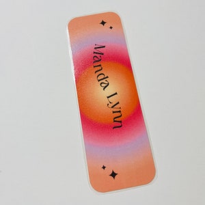 May include: A peach, orange, and pink gradient bookmark with a white border and the name "Manda Lynn" printed in black. The bookmark has two small black stars at the top and bottom.