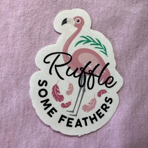 May include: Pink flamingo sticker with the text "Ruffle Some Feathers" and green leaves.