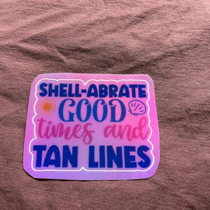 May include: A pink and blue sticker with the text "Shell-abrate good times and tan lines". The sticker has a sun and a seashell graphic.