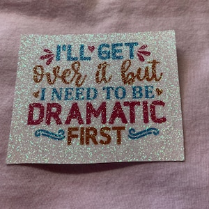 May include: A white iron-on patch with glitter and the text "I'll get over it but I need to be dramatic first" in various colors.