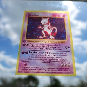 May include: A holographic Mewtwo Pokémon trading card. The card features a purple and white Mewtwo illustration with the text "Mewtwo" at the top. The card's text describes its abilities and stats. The card is 6'7" long and weighs 269 lbs.