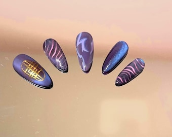 Pode incluir: Cinco unhas postiças em formato de amêndoa em tons de roxo profundo e azul. Os designs incluem um padrão de grade dourada, linhas onduladas rosas, redemoinhos abstratos roxo-claros, um acabamento azul cintilante e linhas rosas.