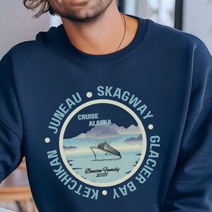May include: A navy blue sweatshirt with a circular graphic design featuring a cruise ship sailing in front of mountains. The text around the graphic reads "Juneau - Skagway - Glacier Bay - Ketchikan" and "Cruise Alaska".