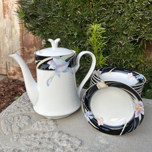 May include: A white teapot with a black and gold floral design and a stack of white bowls with a black and gold floral design.