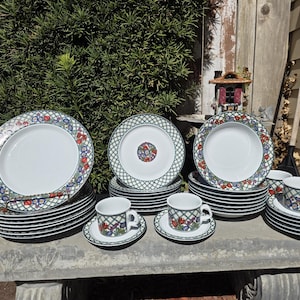 May include: A complete white porcelain dinnerware set with a floral and lattice design. The set includes dinner plates, salad plates, saucers, and cups. The rims of the plates and cups have a green lattice pattern with red and blue floral accents.