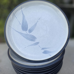 May include: A stack of ceramic plates with a light blue center and a dark blue rim. Each plate features a blue leaf design. The plates are stacked on top of each other.