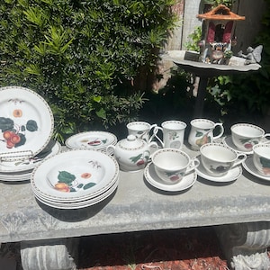 May include: A set of white ceramic dinnerware with a fruit and floral design. The set includes plates, bowls, and a teapot.