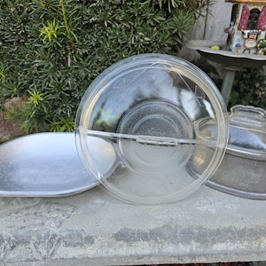 May include: A clear glass divided serving dish with a lid, a silver-colored oval serving dish, and a silver-colored casserole dish with a glass lid. The dishes are on a concrete surface.