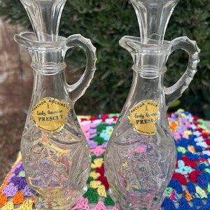 May include: Two clear glass oil and vinegar bottles with gold labels that read "Anchor Hocking Early American Prescut Lancaster Ohio U.S.A."