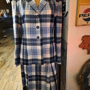 May include: A vintage blue, white, and navy plaid skirt suit. The jacket has a notched collar and three buttons. The skirt is pleated. The suit is displayed on a mannequin.