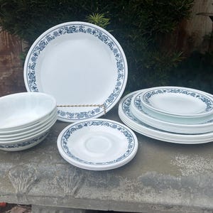 May include: A set of white ceramic dinnerware with a blue floral pattern. The set includes a large dinner plate, a salad plate, a saucer, and a bowl.