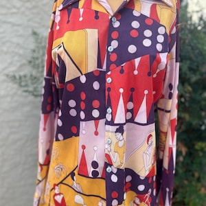 May include: A long-sleeved button-up shirt with a colorful geometric pattern featuring red, yellow, purple, and white. The pattern includes circles, triangles, and abstract figures.