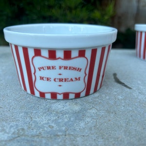 May include: A white ceramic ice cream bowl with red and white stripes. The bowl has a red label that says "Pure Fresh Ice Cream".