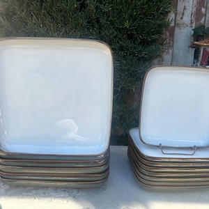 May include: A stack of square ceramic plates with a white glaze and a brown rim. The plates are stacked in two different sizes.