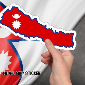 Può includere: Un adesivo rosso e blu con il contorno del Nepal e la bandiera nepalese nell'angolo in alto a sinistra. L'adesivo è tenuto da una mano su uno sfondo bianco e rosso. Il testo "NEPAL MAP STICKER" è stampato sotto l'adesivo.