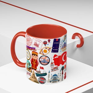 Op de afbeelding: Een keramische mok met een rode handgreep en binnenkant, met een collage van Turkse illustraties. Het ontwerp bevat stempels, bezienswaardigheden, een kaart en de tekst "ISTANBUL" en "MADE IN TURKEY".