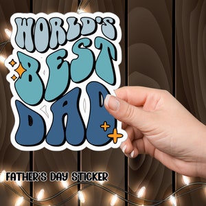 K&ouml;nnte beinhalten: Ein blauer und wei&szlig;er Aufkleber mit dem Text "World's Best Dad" in einer Retro-Schriftart. Der Aufkleber hat ein gelbes Sternendesign und der Text "Father's Day Sticker" ist unter dem Aufkleber gedruckt.