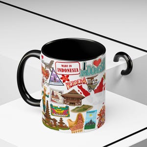 Op de afbeelding: Een witte keramische mok met een zwarte binnenkant en handvat, met een collage van Indonesische afbeeldingen. Het ontwerp bevat postzegels, bezienswaardigheden en de tekst "Made in Indonesia" en "Merdeka".