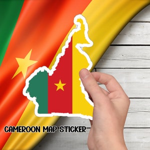 May include: A sticker of the outline of Cameroon with the colors of the Cameroonian flag, red, yellow, and green. The sticker is being peeled off of a wood background.