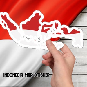 Op de afbeelding: Een witte sticker met een omtrek van de Indonesische eilanden in rood en wit, de kleuren van de Indonesische vlag. De sticker wordt door een hand tegen een witte houten achtergrond gehouden. De tekst "INDONESIA MAP STICKER" is onder de sticker gedrukt.