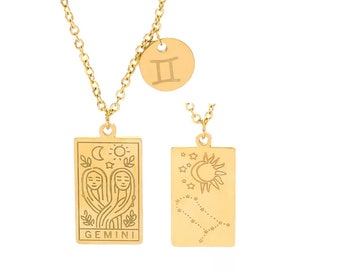 May include: Gold necklace with two pendants. The larger pendant is a rectangular charm with a Gemini zodiac symbol and the words "GEMINI" inscribed. The smaller pendant is a round charm with the Roman numeral "II" inscribed.